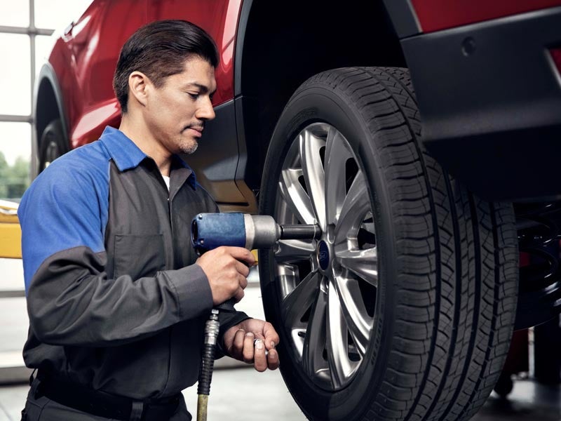 Technician using power tool to tighten lug nuts on a Ford vehicle tire