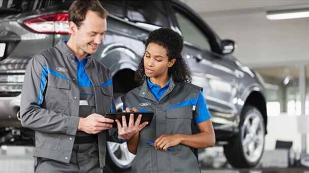 Two Ford technicians reviewing data on a tablet in a service center
