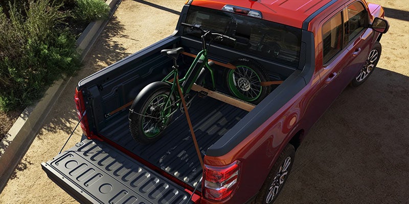 A red pickup truck with a green bicycle secured in its bed using straps. 